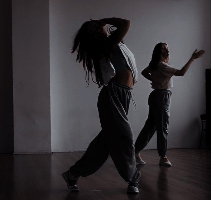Two women exploring movement in a dim dance studio in Bali, heads tilted back, arms reaching.